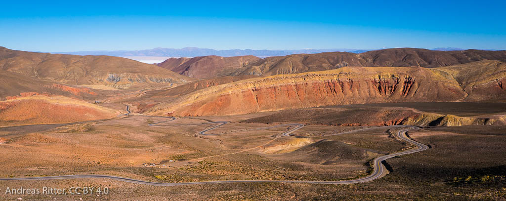 a street meanders through orange-brown treeless mountains